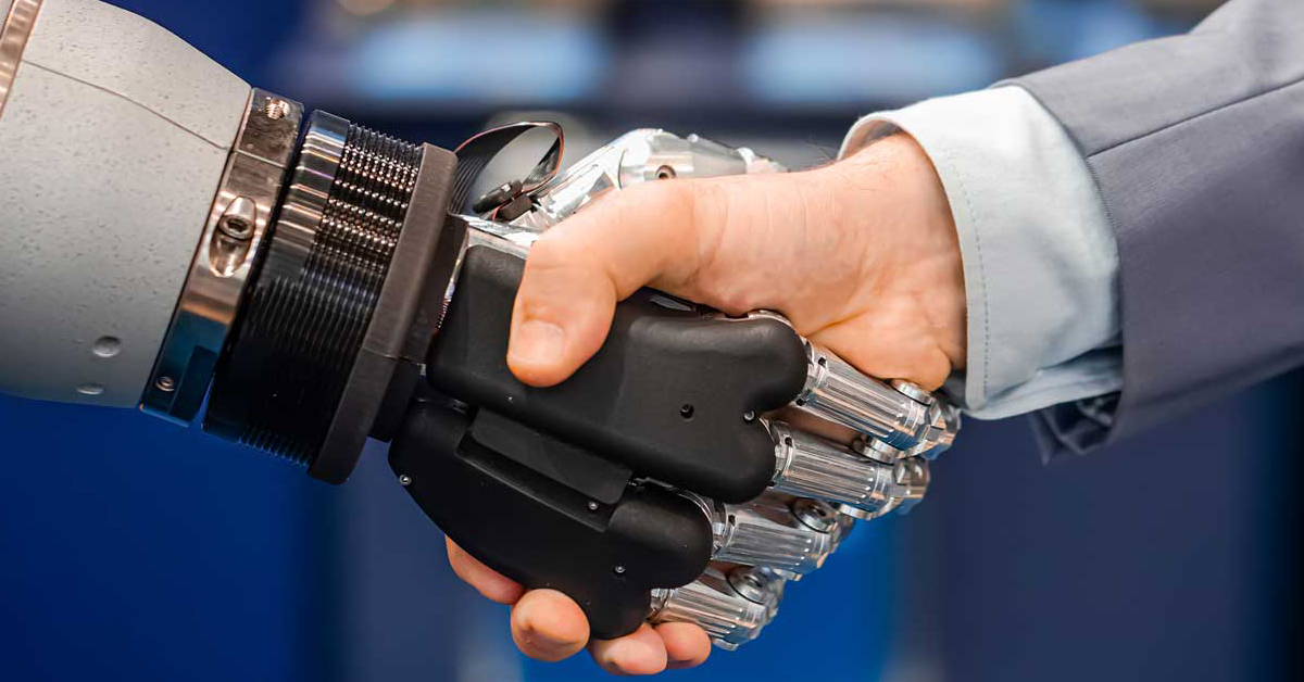 #PraCegoVer: no centro da imagem, mão branca aperta mão de robô como num cumprimento formal.