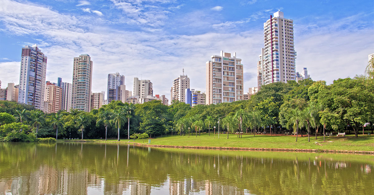 A imagem mostra um parque da cidade de Goiânia. Em primeiro plano há um lado, ao fundo vegetação e prédios.