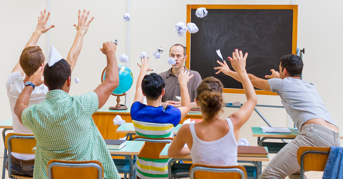 alunos jogando bolas de papel para cima, enquanto professor os assiste em sala de aula.